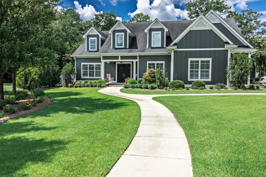 A large gray craftsman new construction house with a landscaped yard and a long leading walkway to the front door