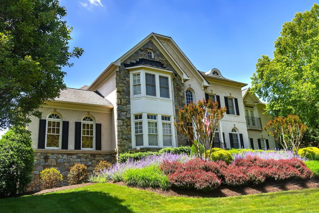 Big luxury house with nicely landscaped front yard and mowed lawn in the suburbs. Summer day, blue sky.